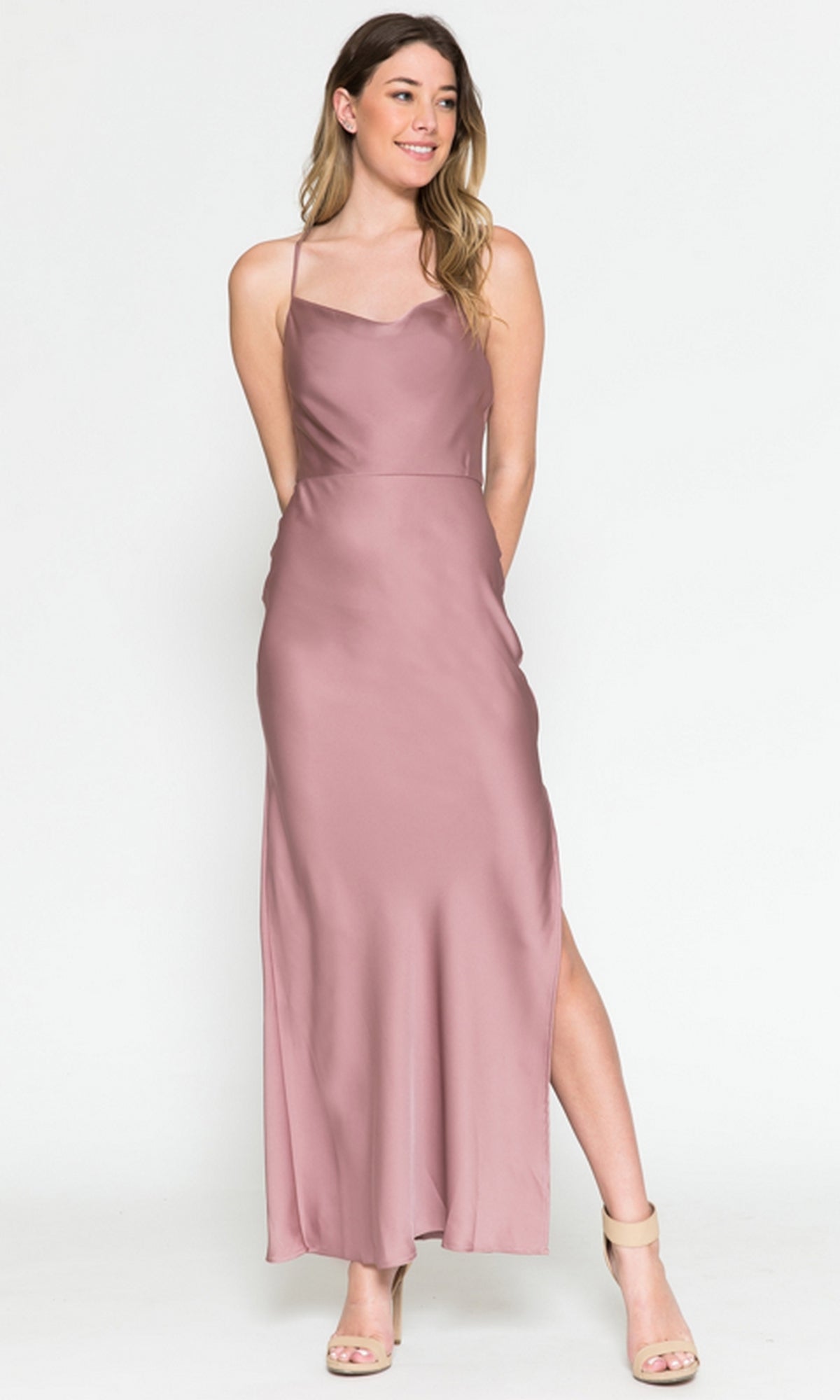 A woman wearing the Cowl-Neck Simple Tea-Length Satin Dress 6115 with a side slit and nude heels stands against a plain white background.